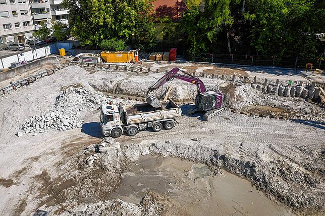 Es geht in die Tiefe: Ein Bagger lädt Erde auf einen Laster, Vorbereitung für den Bau der Tiefgarage.
