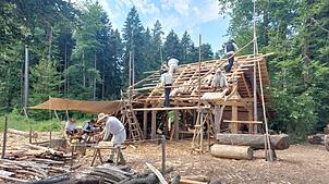 Berufsschüler aus Reutlingen helfen beim Bauen des Dachstuhls. Sie tragen ihre Handwerkskluft mit Hose und Weste, die Ehrenamtlichen und ...