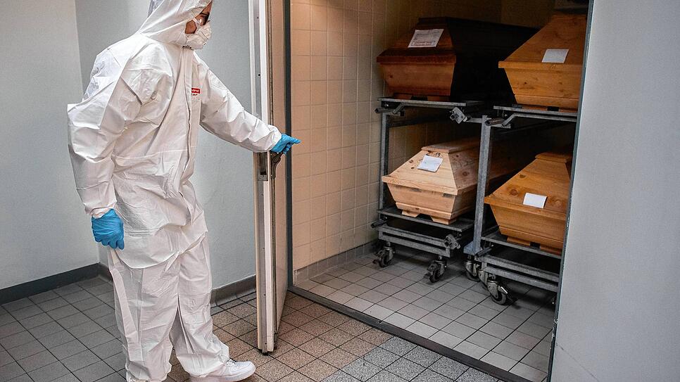 Der Mitarbeiter eines Krematoriums öffnet eine Kühlkammer, in der vier Särge von Verstorbenen stehen, die mit oder an dem Corona-Virus ...