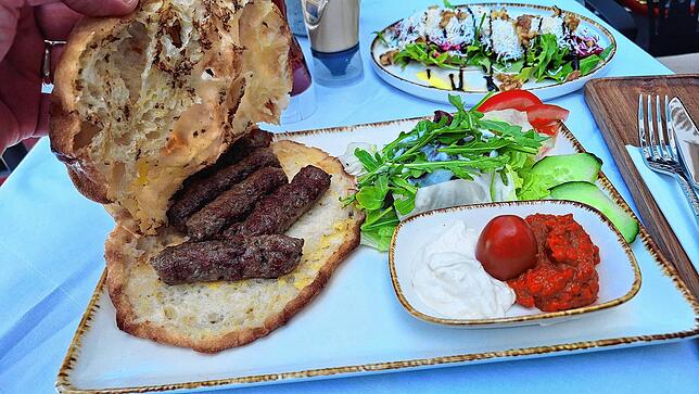 Cevapi mit Beilagen, im Hintergrund der Rote-Beete-Salat.