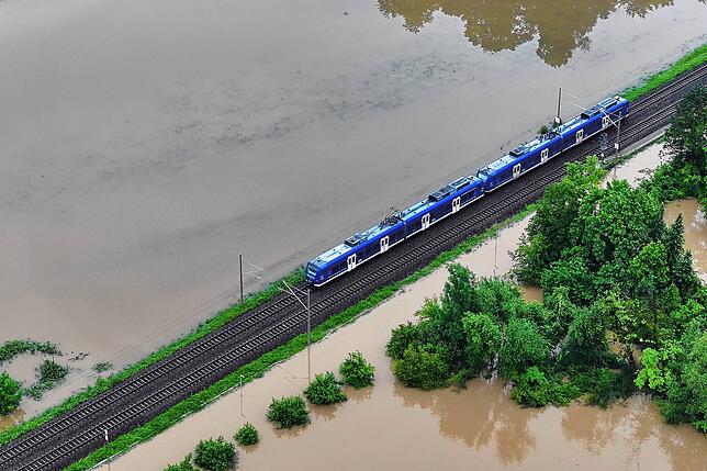 Das Hochwasser des Flusses Schussen überschwemmt Teile von Meckenbeuren. Ein Zug fährt trotz allem über den höhrer gelegenen Bahndamm.