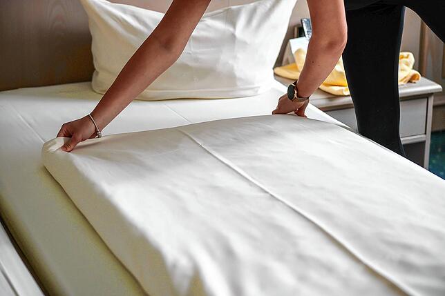Eine Mitarbeiterin eines Hotels streicht eine Bettdecke in einem Hotelzimmer glatt. Auch hier ist der Personalmangel spürbar.