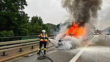 Ein Feuerwehrmitglied löscht das brennende Fahrzeug.