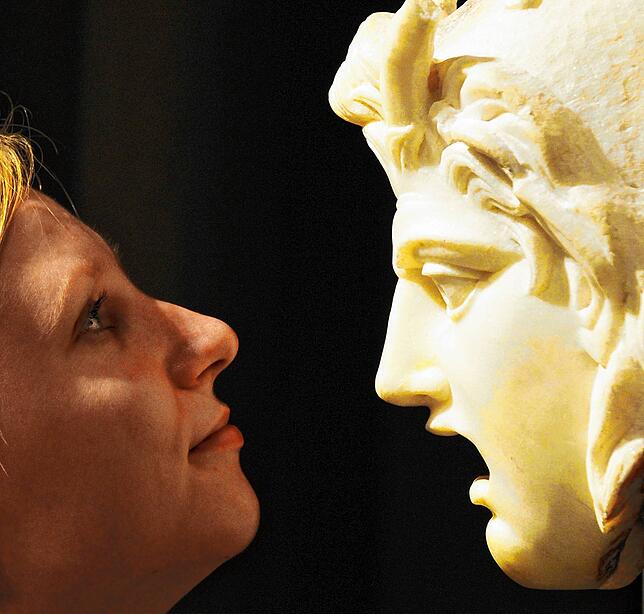 Schau mir in die Augen: Eine Frau betrachtet in einer Ausstellung eine antike Maske, die in der römischen Kaiserzeit entstand.