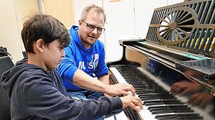Manuel Wagner zeigt dem achtjährigen Louis die Griffe auf dem Klavier.