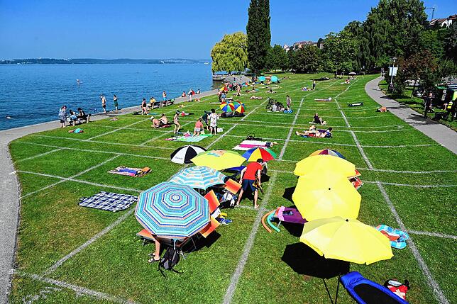 Sonnenbadende liegen an der Uferpromenade auf der Wiese, die die Stadt mit einem Fußballfeld-Streuwagen in Einzelabschnitte aufgeteilt ...