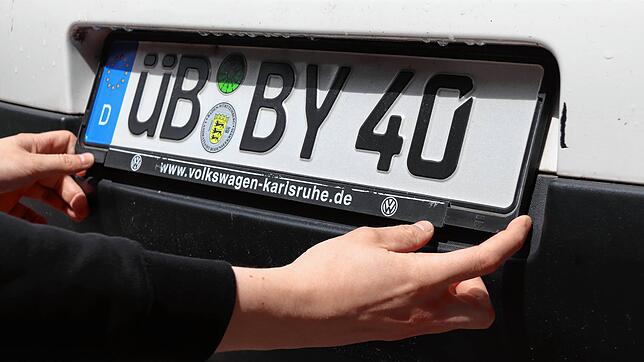 Eine Autofahrerin montiert ein ÜB-Kennzeichen am Heck ihres Autos. Seit Februar 2020 gibt es wieder die Altkennzeichen (Symbolfoto).