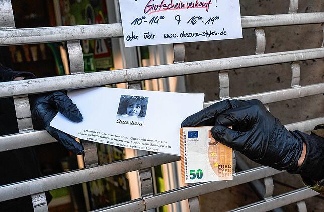 Eine Mitarbeiterin eines Friseursalons in Frankfurt reicht einen „Shutdown-Gutschein“ durch das heruntergelassene Gitter am ...