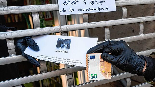 Eine Mitarbeiterin eines Friseursalons in Frankfurt reicht einen &bdquo;Shutdown-Gutschein&ldquo; durch das heruntergelassene Gitter am ...