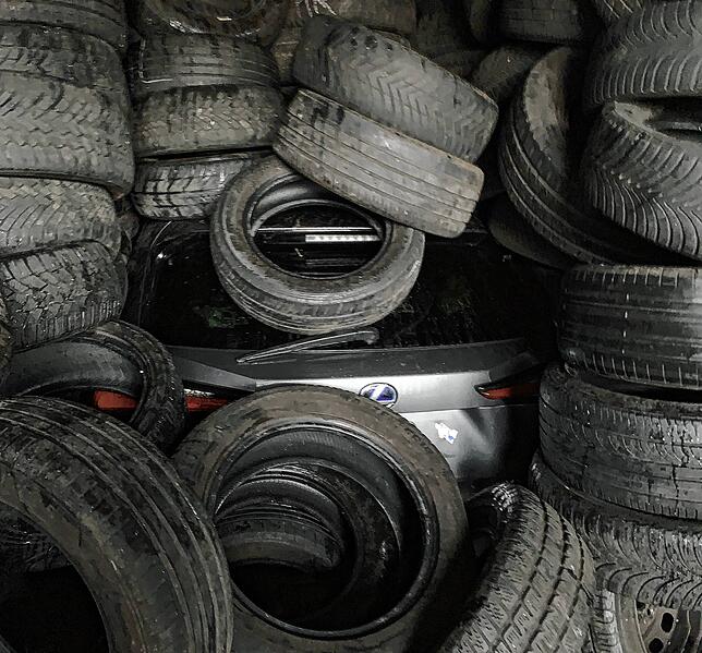 Zwischen alten Autoreifen lugt das Hecks dieses gestohlenen Autos hervor.