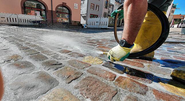 Nach dem Verfugen spritzt ein Mitarbeiter der Baufirma mit einem Schlauch die Pflastersteine ab, um Sand und Fugenmaterial abzuwaschen.