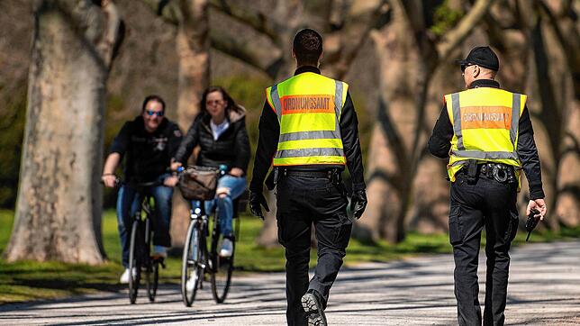 Zwei Mitarbeiter des Ordnungsamts kontrollieren in einem Park die Einhaltung der Schutzmaßnahmen gegen die Verbreitung des Coronavirus.