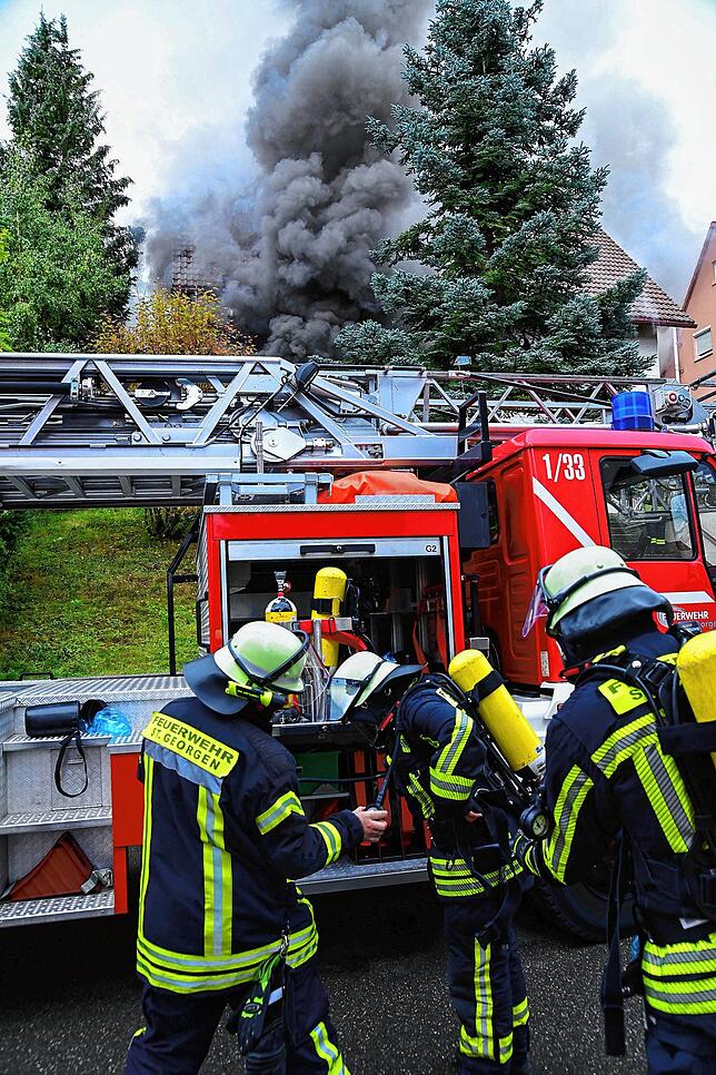 Feuerwehrleute rüsten sich für den Einsatz, im Hintergrund ist die dunkle Rauchwolke zu sehen.