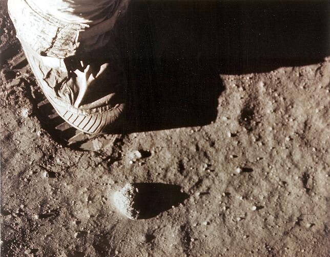Neil Armstrong rechter Fuß tritt in den Mondstaub. Die Abdrücke der Schuhe kann man heute noch sehen.