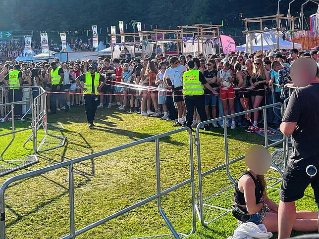 Eine junge Frau sitzt erschöpft am Boden nach dem Gedränge. Im Hintergrund stehen noch viele Menschen an.