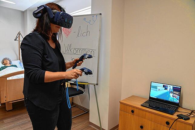 Sabrina Singler steht mit der VR-Brille in der Lerninsel im Lorenzhaus und hantiert virtuell am Pflegebett. Im Hintergrund ist eine ...