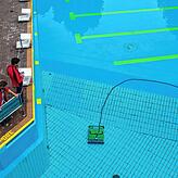 Zwei Mitarbeiter des Schwimmbades stehen am Beckenrand während ein Roboter den Boden eines Schwimmbeckens reinigt. Wenn die Hallenbäder ...