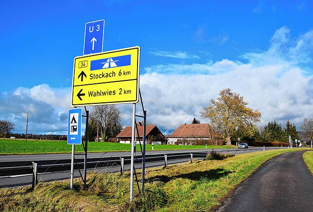 Das Schild weist auf die Abzweigung nach Wahlwies am Mooshof im Hintergrund hin. Auf dieser Seite der B34 ist ein Radweg, auf der ...