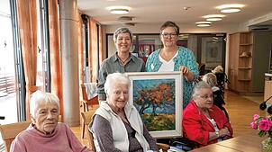 Annette Loll vom Kulturring und Martina Meier (stehend von links) mit einem Werk von Ingrid Veit. Die Bewohnerinnen freuen sich ...