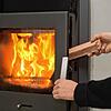 Ein Mann legt in seinen Kaminofen ein Stück Holz nach, um das Feuer zu halten. Ältere Geräte dürfen nur noch bis Ende des Jahres genutzt ...