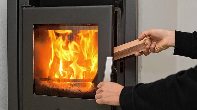 Ein Mann legt in seinen Kaminofen ein Stück Holz nach, um das Feuer zu halten. Ältere Geräte dürfen nur noch bis Ende des Jahres genutzt ...