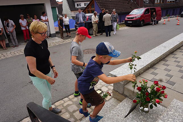Lehrerin Dorothea Schlatter kommt mit Schülern, die am Stolperstein rote rosen niederlegen.