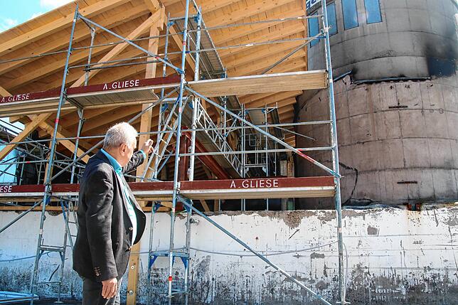 Niederlassungsleiter Michael Rau zeigt auf Gerüste, die das provisorische Dach des abgebrannten Gebäudeelementes stützen.