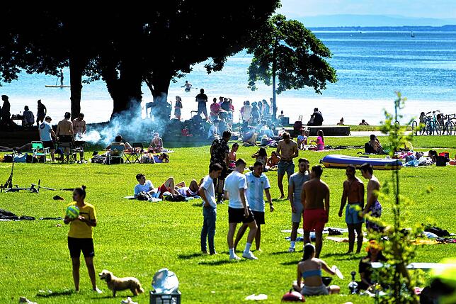 Parkbesucher sitzen zusammen, grillen, und genießen das warme Frühlingswetter am Ufer des Genfer Sees: Größere Gruppen sind draußen kein ...
