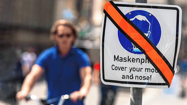 Die Masken-Regel gilt in vielen Bereichen nicht mehr: Ein mit orangenem Klebeband durchgestrichenes Hinweisschicht zur Maskenpflicht ...