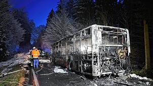 Feuerwehrleute stehen neben einem ausgebrannten Bus. Der Linienbus ist bei Mittelbiberach in Brand geraten.