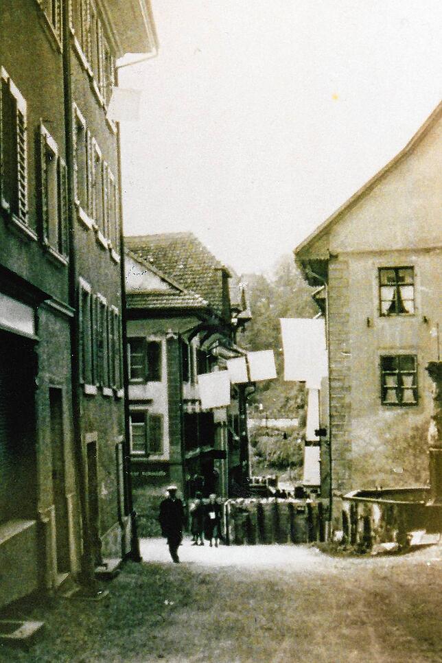 Die untere Hauptstraße im April 1945: Aus den Fenstern hängen zum Zeichen der kampflosen Übergabe der Stadt weiße Flaggen. Am Mittleren ...