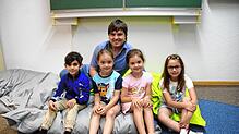 Björn Tscharntke und je zwei Kinder aus der Vorschulgruppe und der ersten Klasse auf einem Riesenkissen im Buchstabenraum. Nun zieht es ...