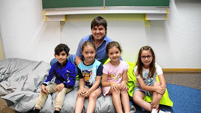 Björn Tscharntke und je zwei Kinder aus der Vorschulgruppe und der ersten Klasse auf einem Riesenkissen im Buchstabenraum. Nun zieht es ...