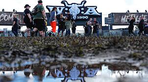 Metal-Fans gehen über das teilweise matschige Festivalgelände des Wacken Open Airs (WOA). Die Anreise zu einem der größten ...