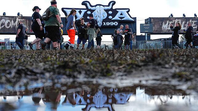 Metal-Fans gehen über das teilweise matschige Festivalgelände des Wacken Open Airs (WOA). Die Anreise zu einem der größten ...
