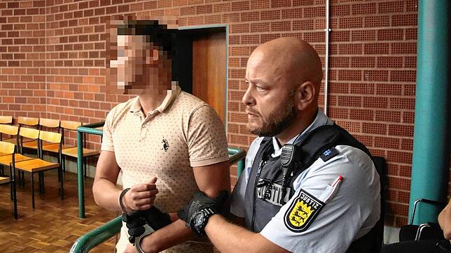 Einer der Angeklagten wird vor Prozessbeginn gefesselt in den Verhandlungssaal geführt.