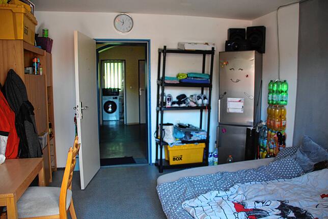Das Zimmer des Paares mit Matratzen, Tisch, Schrank und Kühlschrank.