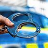Eine Hand hält Handschellen vor einen Streifenwagen der Polizei (Symbolbild). Seiner Verhaftung entging ein 26-Jähriger in Basel &ndash; ...