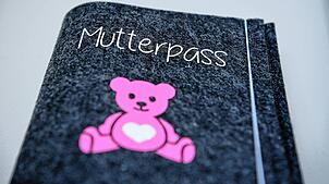 Ein Mutterpass mit einem pinkfarbenen Teddybären. Nun sollen auch Frauen, die ab der 13. Schwangerschaftswoche eine Fehlgeburt erleiden, ...