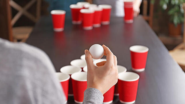 Landet der Ball im gegnerischen Becher, muss der Kontrahent austrinken. So geht Bierpong. Bild: Africa Studio/Adobe Stock