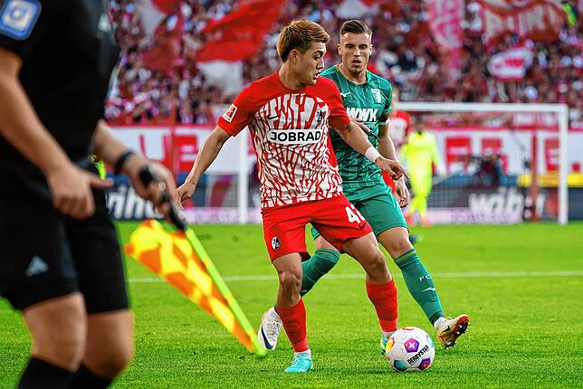 Der Freiburger Ritsu Doan (M) im Zweikampf mit dem Augsburger und ehemaligen Freiburger Ermedin Demirovic (r).