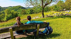 Zwei Wanderer machen auf einer Bank auf der Schwäbischen Alb eine Pause.