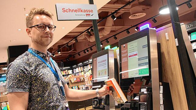 Lukas Herberth, Leiter der Thalia-/Osiander-Filiale im Lago-Einkaufszentrum in Konstanz, zeigt, wie eine Selbstscan-Kasse funktioniert. ...