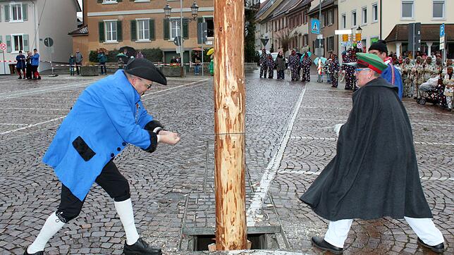 Narrenvater &bdquo;Hubert I.&ldquo; Rössler und Narrenbolizei Michael Bauer sägen am Stamm des Narrenbaums. Im Hintergrund links spannen ...