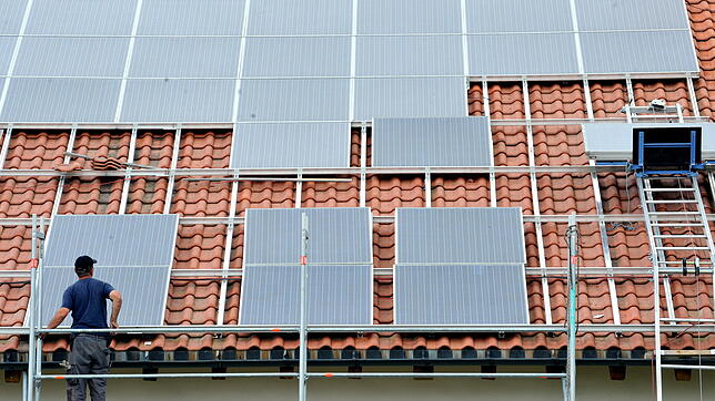 Ein Arbeiter installiert auf einem Dach eine Solaranlage zur Stromerzeugung. Weil das Ausbauziel der Bundesregierung bald erreicht ist, ...