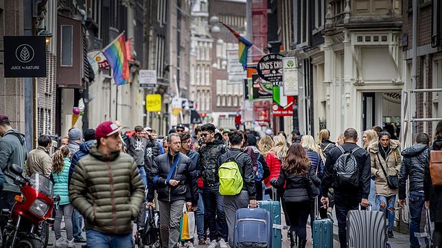 Touristen laufen mit Rollkoffern durch das Zentrum von Amsterdam. Die Stadt hat nun die Neubebauung von Hotels eingeschränkt und ...