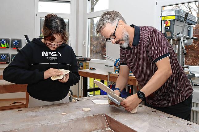 Mit ihrem Vater Matthias Flath schleift Stella in der Holzwerkstatt an einer Holzsägearbeit.