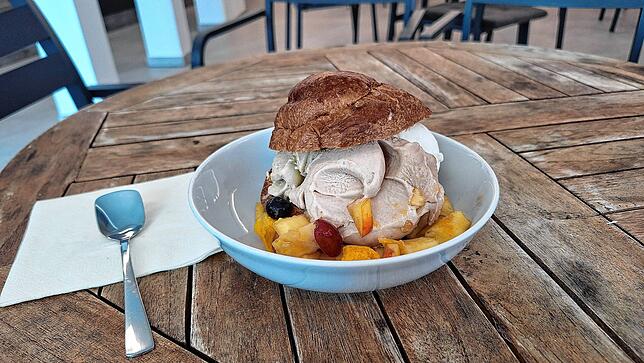 Brioche mit drei Kugeln Eis und Obststücken.