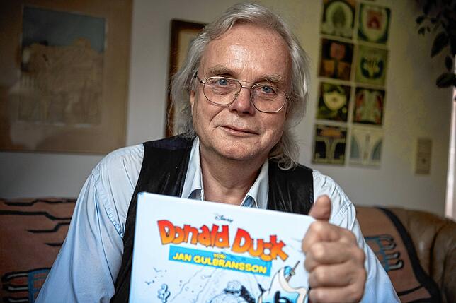 Jan Gulbransson sitzt mit einem Sammelband seiner Comics in seiner Wohnung in München. Dieses Foto entstand 2016, damals zeichnete ...