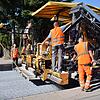 Eine spezielle Konstruktion am Straßenfertiger streut das Abstreumaterial für den Hightech-Asphalt (Mitte unten) auf den heißen Asphalt ...